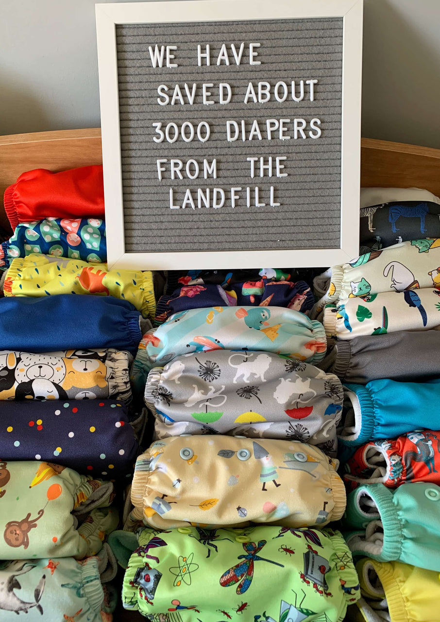 a stack of colored reusable diapers with a sign that says, “We have saved about 3,000 diapers from the landfill”