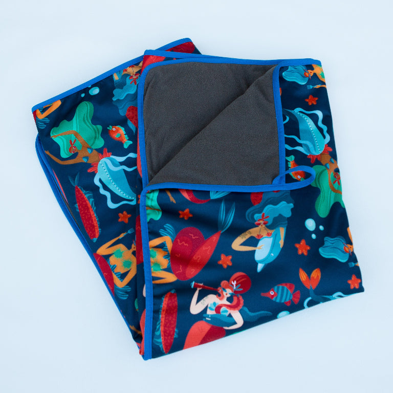 Colorful blanket with mermaid and ocean-themed illustrations on a light background.