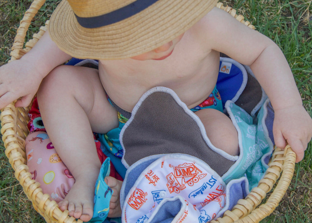 basket with cloth diapers inserts and baby wearing a hat